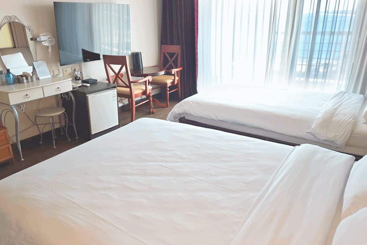 Een hotelkamer met twee bedden, een bureau met computer, een stoel en een groot raam met gordijnen.