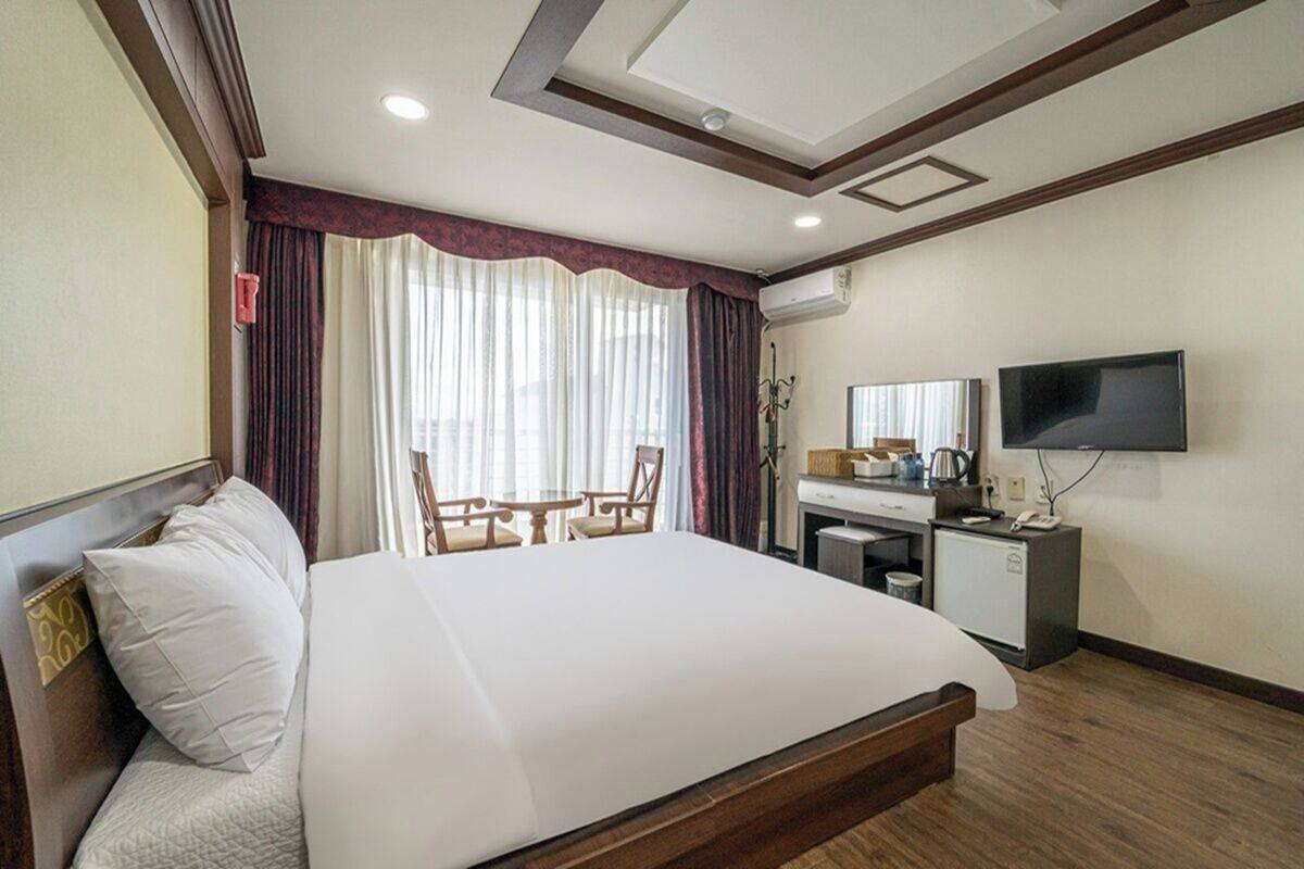 Een hotelkamer met een bed, bureau, stoel, televisie en een raam met gordijnen.