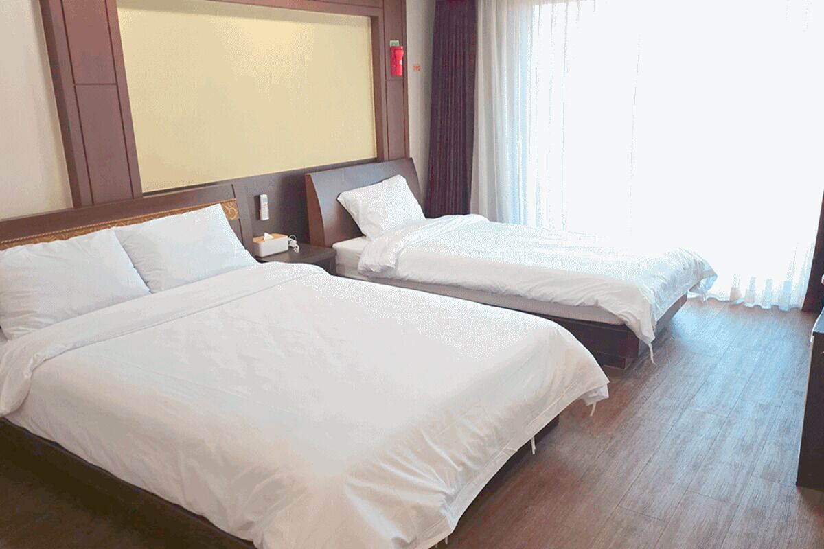 Habitación de hotel con dos camas, una mesita de noche y un ventanal con cortinas.