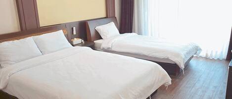 Habitación de hotel con dos camas, una mesita de noche y un ventanal con cortinas.