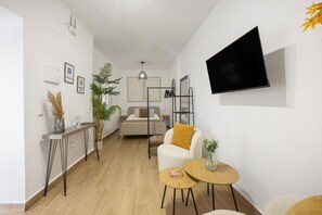 Ein modernes Wohnzimmer mit einer Couch, einem Couchtisch, einem an der Wand montierten Fernseher und einem Bett im Hintergrund.