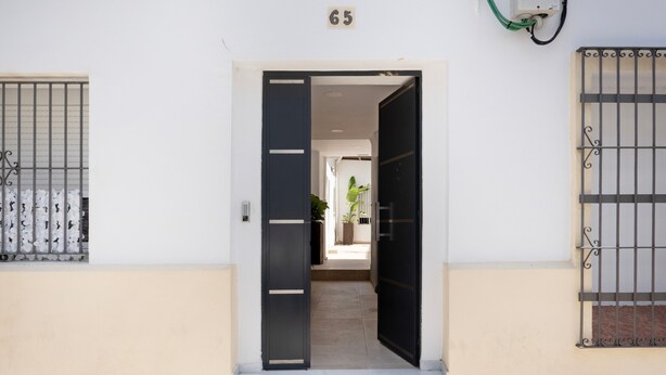 A building entrance with a number '65' above the door, a metal gate on the left, and a similar gate on the right. - Mamalú Apartment: New, Romantic & Central in Jerez (Jerez de la Frontera)