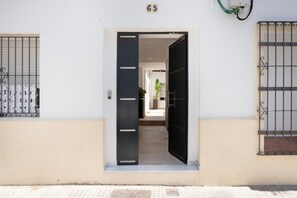 Entrada de un edificio con el número '65' sobre la puerta, una verja metálica a la izquierda y otra similar a la derecha.
