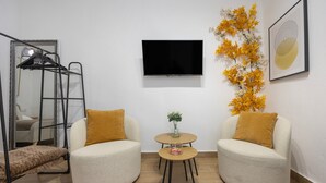 A modern room with two armchairs, a small table, a TV, a mirror, and a decorative plant. - Mamalú Apartment: New, Romantic & Central in Jerez (Jerez de la Frontera)