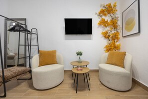 Ein modernes Zimmer mit zwei Sesseln, einem kleinen Tisch, einem Fernseher, einem Spiegel und einer Zimmerpflanze.