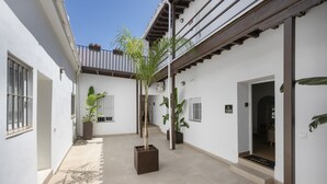 A courtyard with potted plants, a tiled floor, and a door leading to a room. - Mamalú Apartment: New, Romantic & Central in Jerez (Jerez de la Frontera)