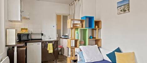 Habitación pequeña con cama, escritorio, kitchenette y baño.