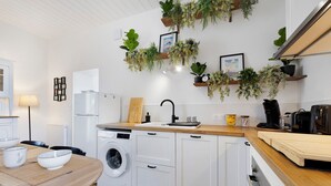 A modern kitchen with a washing machine, wooden countertop, white cabinets, and hanging plants.