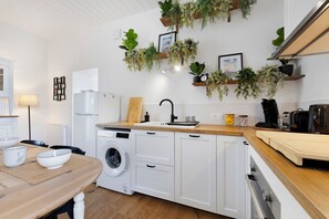 Eine moderne Küche mit Waschmaschine, Holz Arbeitsplatte, weißen Schränken und hängenden Pflanzen.