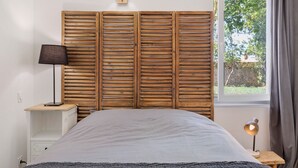 A bedroom with a bed, a nightstand, a lamp, a wall-mounted light, and a window with curtains.