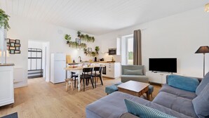 Ein modernes Wohnzimmer mit grauem Sofa, einem Fernseher und einem Essbereich mit Küche im Hintergrund.