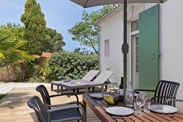 A wooden deck with a table and chairs, a bottle, glasses, and a bowl of fruit.