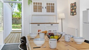 A kitchen with white cabinets, a dining table with white bowls and mugs, and a view of the outdoors.