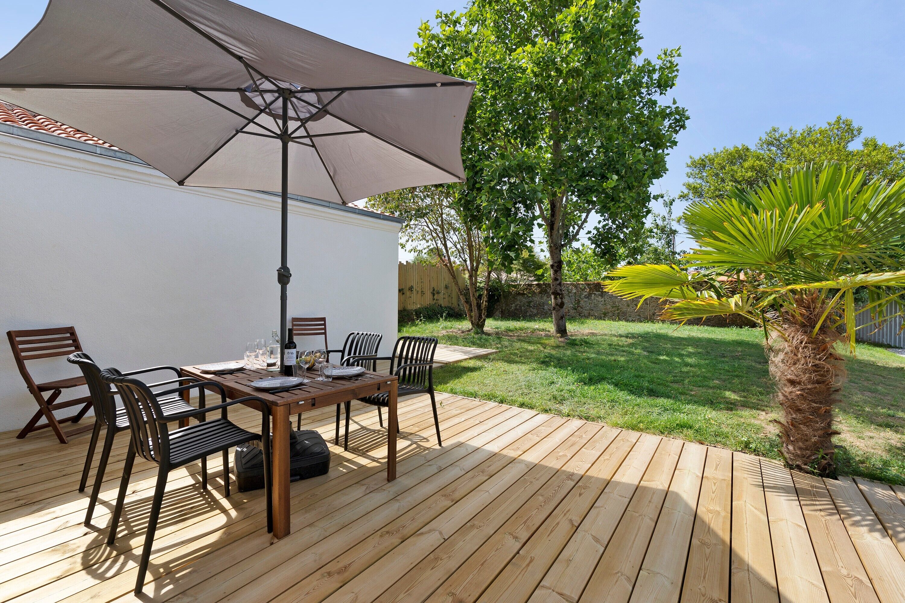 A wooden deck with a table and chairs, a large umbrella, and a palm tree.