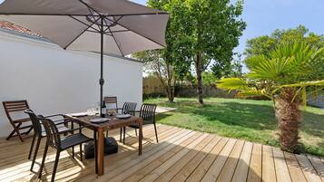 A wooden deck with a table and chairs, a large umbrella, and a palm tree.