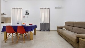 Ein Zimmer mit Esstisch, Stühlen, einer Couch und Vorhängen.
