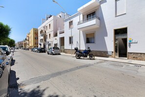 A street with parked cars and a motorcycle, buildings with balconies, and a clear sky. - Room 'Camera Matrimoniale Sabrina' with Wi-Fi and Air Conditioning (Alghero)