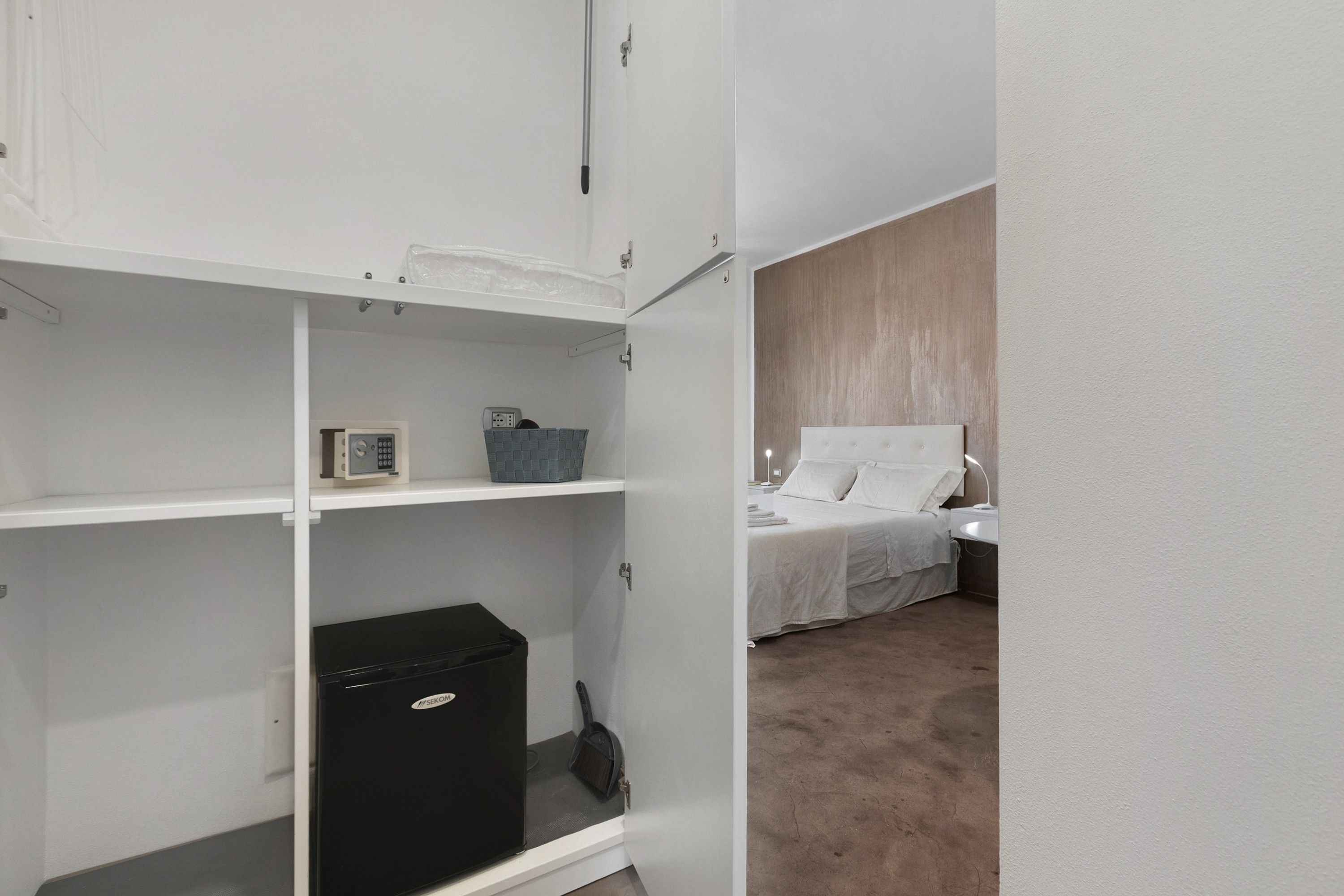 A hotel room with a bed, a nightstand, a lamp, and a wardrobe with a small appliance.