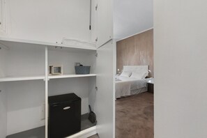 Habitació d'hotel amb un llit, una tauleta de nit, una làmpada i un armari amb un aparell petit.