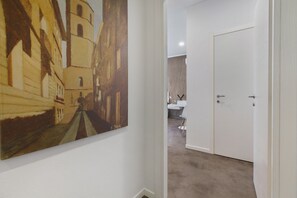 A hallway with a painting of a building, a white door, and a bathroom visible in the background. - Room 'Camera Matrimoniale Sabrina' with Wi-Fi and Air Conditioning (Alghero)