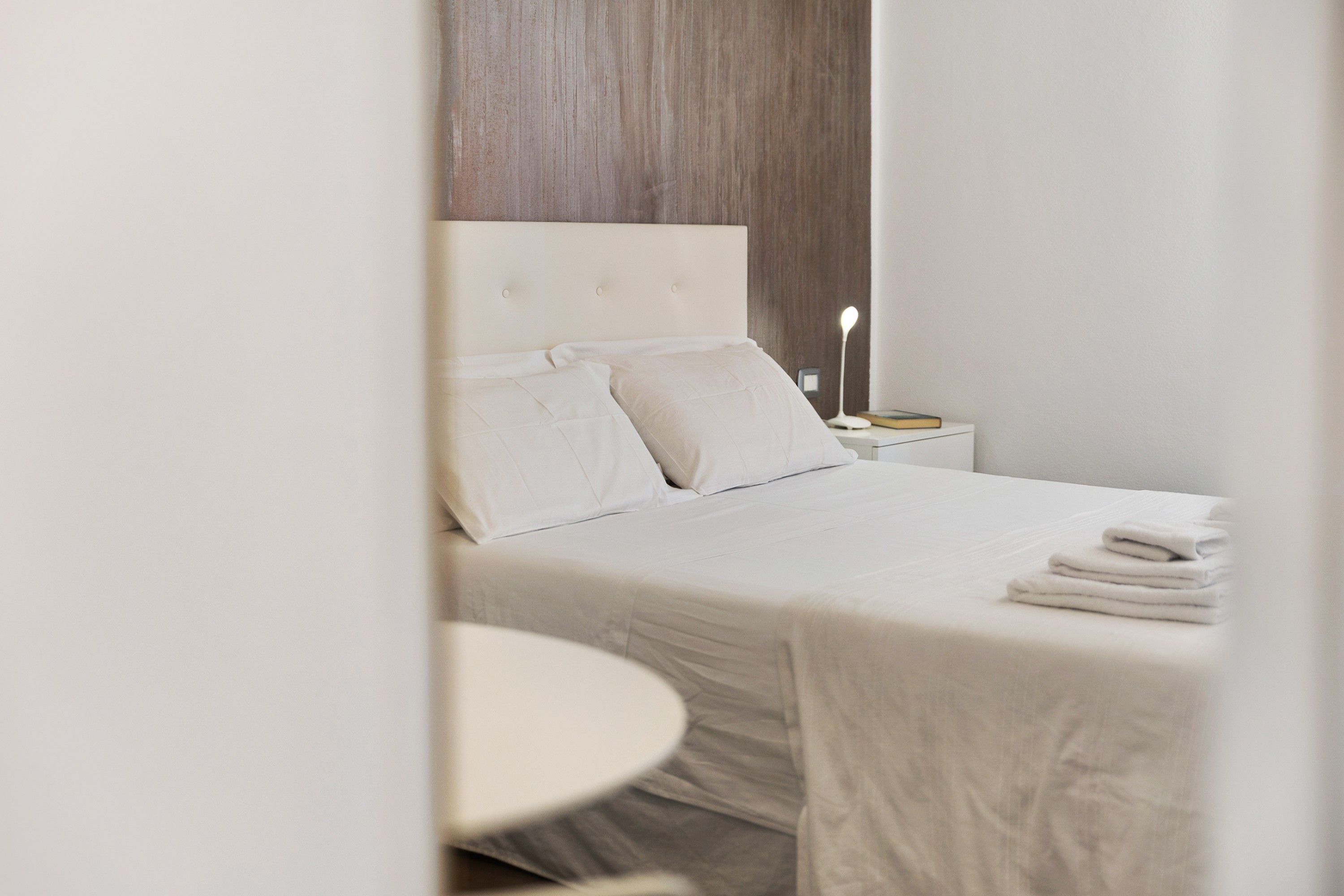 A neatly made bed with a headboard, a bedside table with a lamp, and a round table.