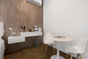 Ein moderner, minimalistischer Raum mit einer Wand in Holzoptik, einem weißen Schreibtisch mit Lampe, einem kleinen Tisch mit Stühlen und einem Papierkorb.