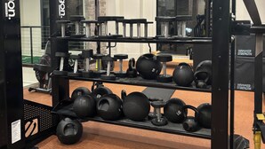 Une salle de sport équipée de matériel de musculation, notamment des haltères et des balles lestées, et dotée d’un mur recouvert de miroirs.