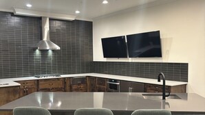 Une cuisine moderne dotée d’un grand îlot central, de tabourets de bar, d’une hotte en acier inoxydable et de deux téléviseurs à écran plat fixés au mur.