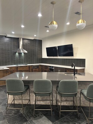 A modern kitchen with a large island, bar stools, a stainless steel range hood, and two flat-screen TVs mounted on the wall. - Luxury/Cozy 1-Bedroom Condo Retreat Dunwoody GA (Dunwoody)