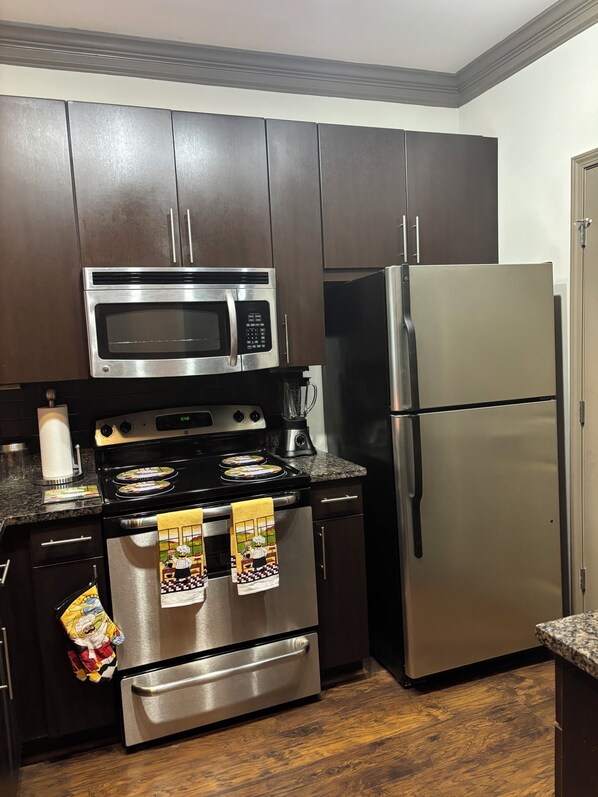 A kitchen with dark cabinets, a stainless steel microwave, oven, and refrigerator.