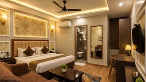 A hotel room with a bed, a sofa, a desk, a mirror, and a ceiling fan. - HOTEL MUDITA BY KIRTI (Patna)