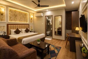 A hotel room with a bed, a sofa, a desk, a mirror, and a ceiling fan. - HOTEL MUDITA BY KIRTI (Patna)