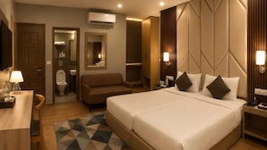 A hotel room with a large bed, a desk, a chair, a sofa, a bathroom, and a TV. - HOTEL MUDITA BY KIRTI (Patna)
