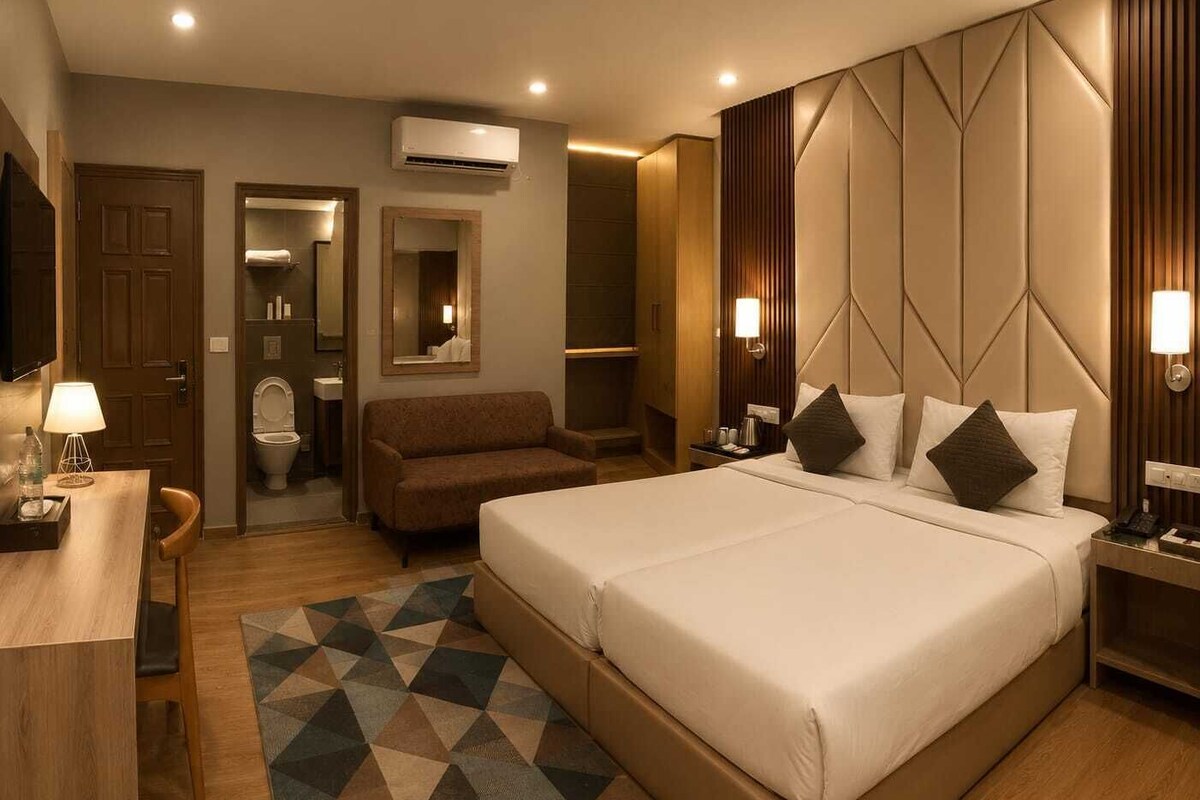 A hotel room with a large bed, a desk, a chair, a sofa, a bathroom, and a TV.