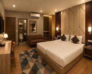 A hotel room with a large bed, a desk, a chair, a sofa, a bathroom, and a TV. - HOTEL MUDITA BY KIRTI (Patna)