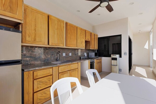 Una cocina moderna con armarios de madera, encimera de granito, ventilador de techo y comedor con mesa y sillas blancas.