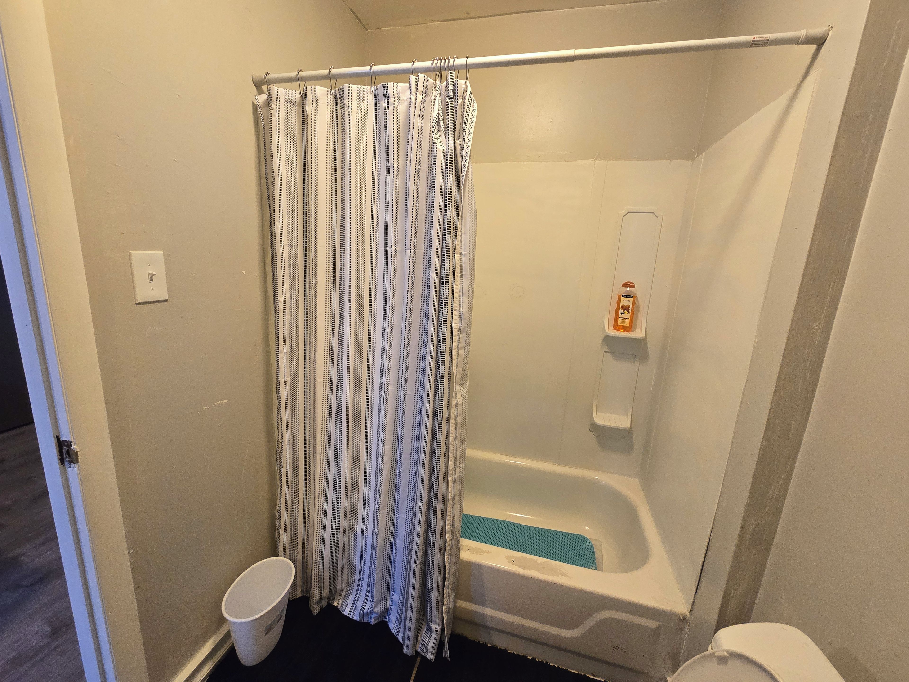 A bathroom with a shower curtain, a bathtub, a toilet, and a soap dispenser.