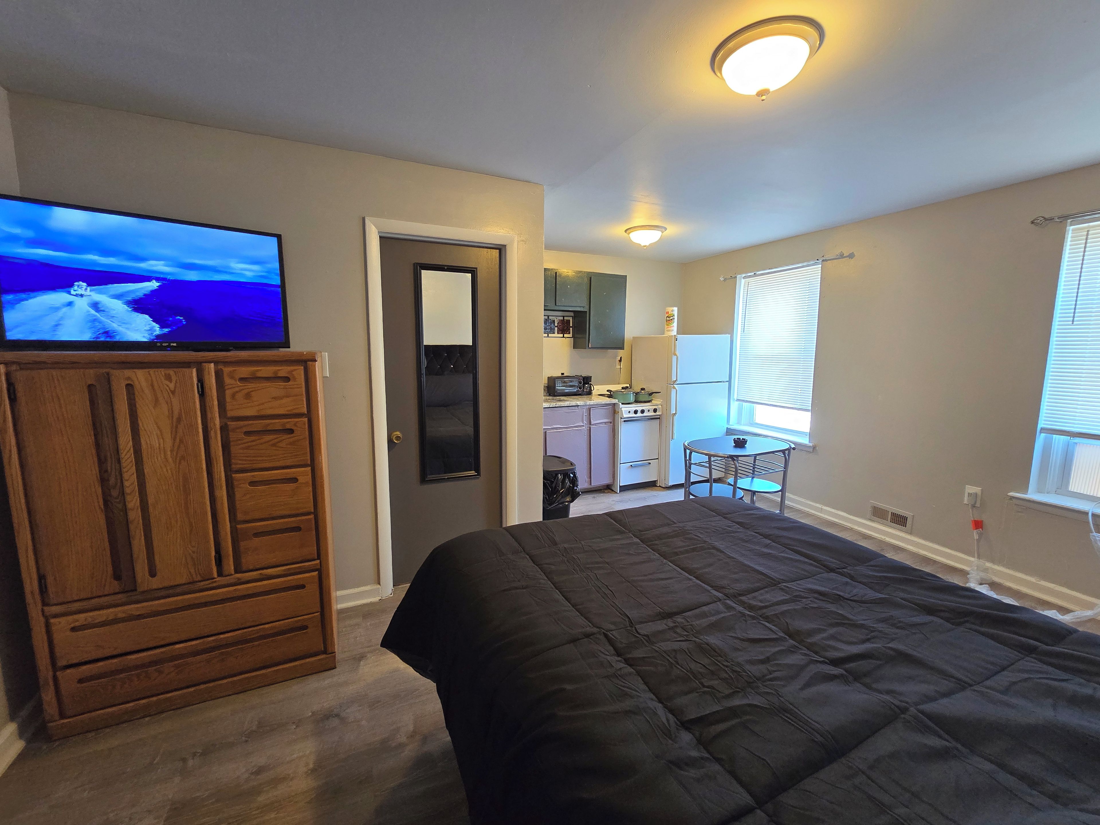Een slaapkamer met een bed, een houten dressoir, een televisie en een keuken op de achtergrond.