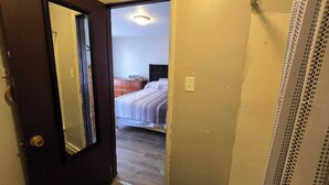 Une porte qui mène à une chambre à coucher, où se trouvent un lit, une commode et un luminaire au plafond.