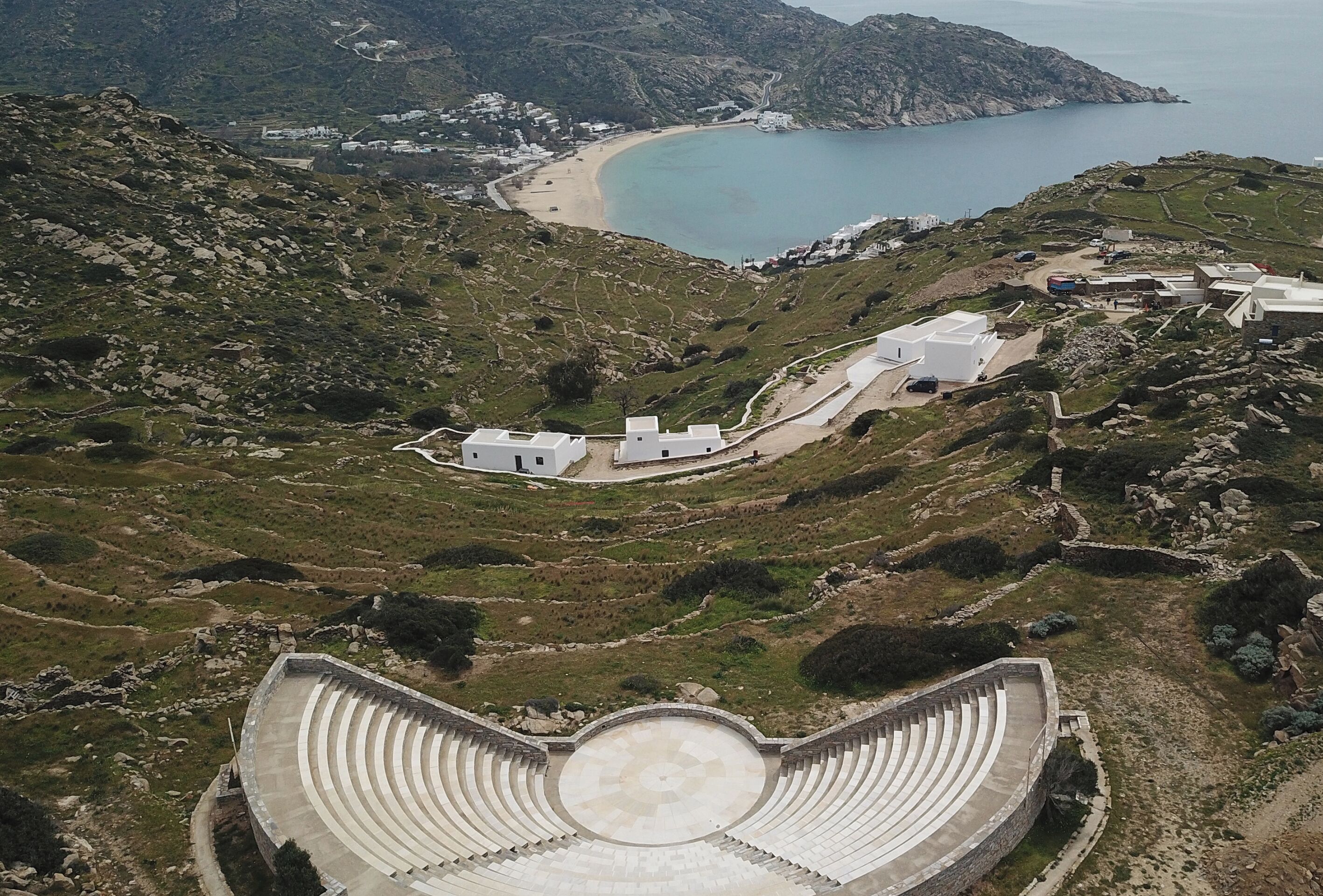 Un anfiteatro con asientos escalonados, vista al mar y edificios dispersos.