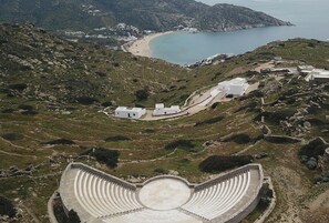 An amphitheater with tiered seating, a coastal view, and scattered buildings.