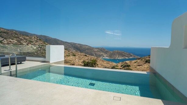 A modern pool with clear blue water, surrounded by white walls, overlooking a rugged coastline and the sea.