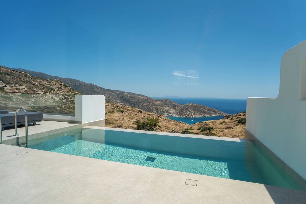 A modern pool with clear blue water, surrounded by white walls, overlooking a rugged coastline and the sea.