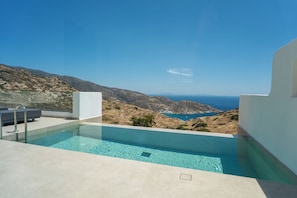 Ein moderner Pool mit klarem, blauem Wasser, umgeben von weißen Wänden, mit Blick auf eine zerklüftete Küstenlinie und das Meer.