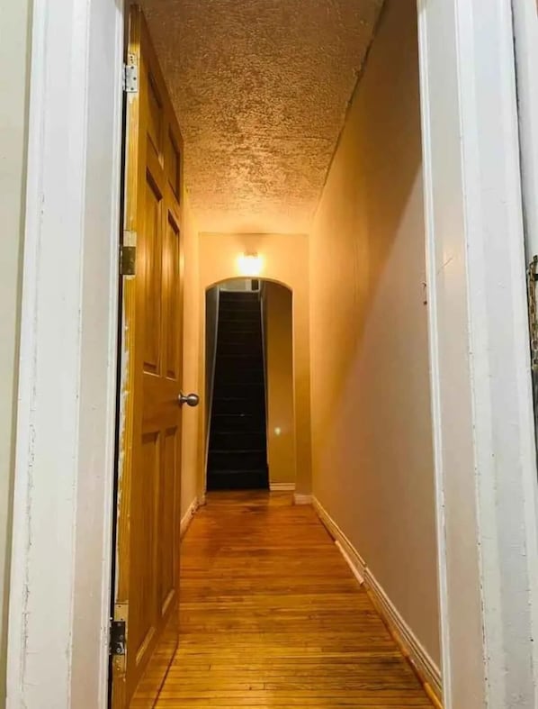 A narrow hallway with wooden flooring, white walls, and a door at the end.