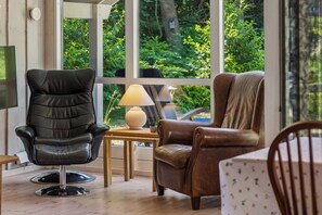Ein Zimmer mit großem Fenster, einem schwarzen Ledersessel, einem braunen Ledersessel, einem kleinen Tisch mit Lampe und einem Holzstuhl.