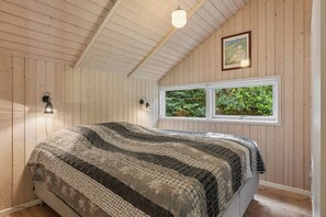 Ein Schlafzimmer mit einem Bett, Holzwänden, einem Fenster mit Blick auf Grünflächen und einem Gemälde an der Wand.