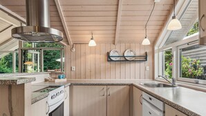 Une cuisine dotée de meubles en bois, d’une hotte de cuisinière en acier inoxydable, d’un lave-vaisselle et d’une fenêtre donnant sur un paysage verdoyant.