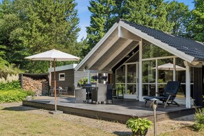 Ein modernes Haus mit einer Terrasse, Sitzgelegenheiten im Freien und einem großen Panoramafenster.