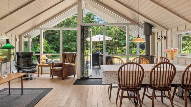 Une pièce spacieuse et bien éclairée, dotée d’un plafond haut, de grandes fenêtres et d’un coin repas avec des chaises et une table en bois.